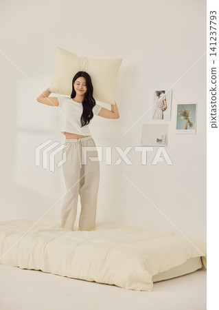 Woman stretching with a pillow in a bright minimal bedroom 141237793