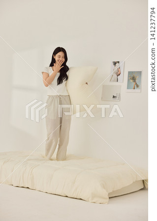 Asian woman posing with a pillow in a white bedroom 141237794