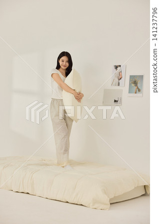 Woman stretching with a pillow in a bright minimal bedroom Woman stretching with a pillow in a bright minimal bedroom 141237796