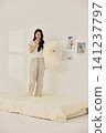 Young Asian woman standing on a bed and holding a large pillow 141237797