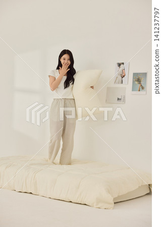 Young Asian woman standing on a bed and holding a large pillow Young Asian woman standing on a bed and holding a large pillow 141237797