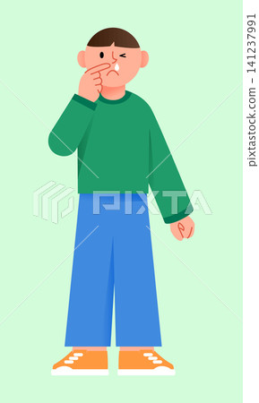 A boy stands in a basic green background. He makes a funny face and holds his nose with one hand. The boy looks to be in a playful mood. 141237991