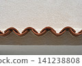 Wavy clay roof tiles meeting a textured white plaster wall. 141238808