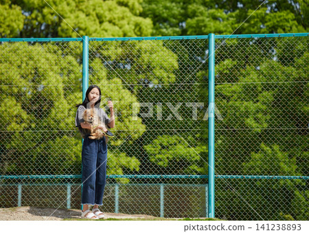 A teenage girl in casual clothes is seen walking in a park in spring, carrying a cute Pomeranian puppy. A teenage girl in casual clothes is seen walking in a park in spring, carrying a cute Pomeranian puppy. 141238893