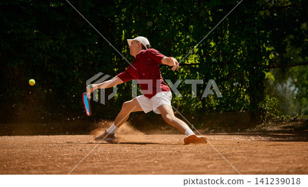 Tennis player stretching wide for forehand return on dusty clay court. Tennis player stretching wide for forehand return on dusty clay court. 141239018