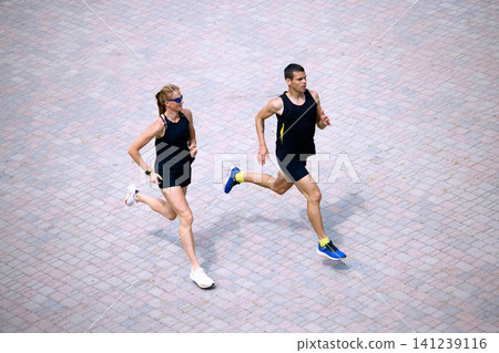 Urban couple jogging in top view on tiled pavement. Urban couple jogging in top view on tiled pavement. 141239116