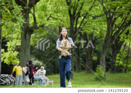 A teenage girl is seen happily walking her cute Pomeranian puppy in a park in springtime. A teenage girl is seen happily walking her cute Pomeranian puppy in a park in springtime. 141239120