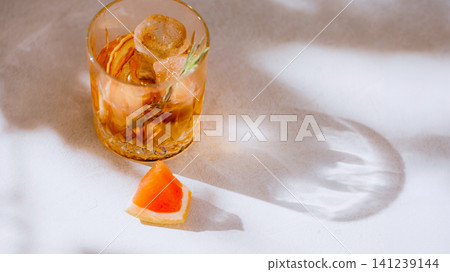 Amber grapefruit cocktail with rosemary, ice and large sunlight shadow copy space. Amber grapefruit cocktail with rosemary, ice and large sunlight shadow copy space. 141239144