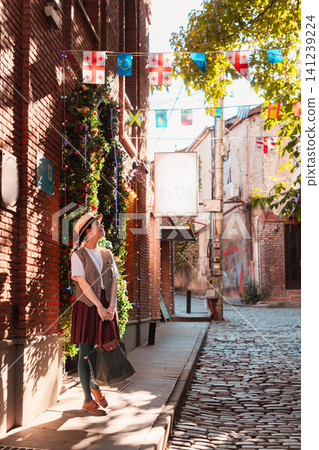 Woman standing by a red brick wall under Georgian flags and fairy lights. Vertical Woman standing by a red brick wall under Georgian flags and fairy lights. Vertical 141239224
