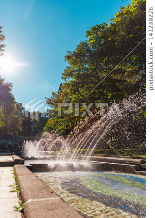 Sunny park fountain with multiple water jets splashing against a bright blue sky. Vertical Sunny park fountain with multiple water jets splashing against a bright blue sky. Vertical 141239228
