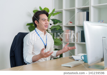Asian businessman wearing headset gesturing during video call in office Asian businessman wearing headset gesturing during video call in office 141239596