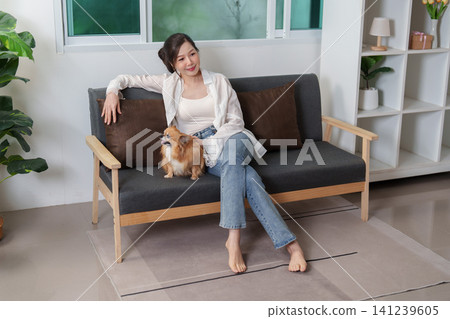 Asian woman relaxing on sofa with Chihuahua dog at home 141239605