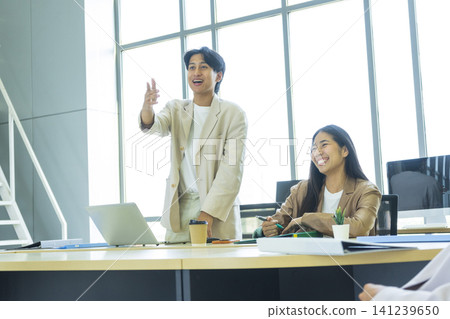 Young cheerful Asian business woman discussing project with colleagues while working together in the modern office. Young cheerful Asian business woman discussing project with colleagues while working together in the modern office. 141239650