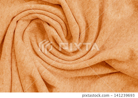 Horizontal macro close up of a soft pastel orange knitted fabric material texture twisted into a beautiful spiral swirl pattern on a warm cozy sweater 141239693