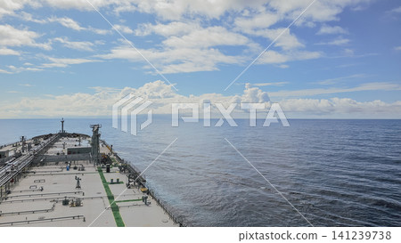 High angle view of a massive cargo ship deck sailing through calm blue ocean water under a beautiful bright sky with fluffy white clouds on a sunny day High angle view of a massive cargo ship deck sailing through calm blue ocean water under a beautiful bright sky with fluffy white clouds on a sunny day 141239738