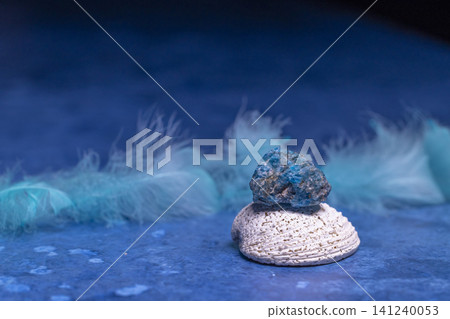 Blue apatite crystal balancing on seashell with feathers Blue apatite crystal balancing on seashell with feathers 141240053