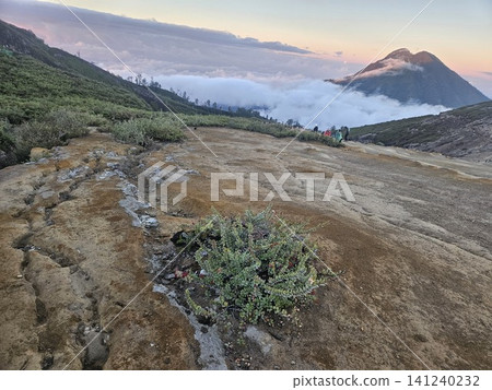 The stunning panoramic sunrise view of the turquoise acid crater lake at Mount Ijen volcano, featuring majestic rocky mountain ridges and thick sulfur smoke rising from the active vents in East Java. The stunning panoramic sunrise view of the turquoise acid crater lake at Mount Ijen volcano, featuring majestic rocky mountain ridges and thick sulfur smoke rising from the active vents in East Java. 141240232