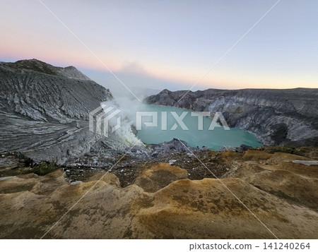 The stunning panoramic sunrise view of the turquoise acid crater lake at Mount Ijen volcano, featuring majestic rocky mountain ridges and thick sulfur smoke rising from the active vents in East Java. The stunning panoramic sunrise view of the turquoise acid crater lake at Mount Ijen volcano, featuring majestic rocky mountain ridges and thick sulfur smoke rising from the active vents in East Java. 141240264