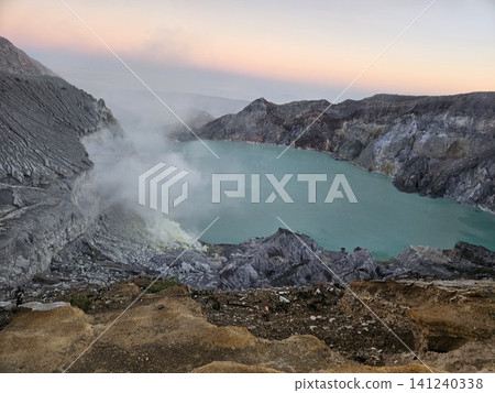 The stunning panoramic sunrise view of the turquoise acid crater lake at Mount Ijen volcano, featuring majestic rocky mountain ridges and thick sulfur smoke rising from the active vents in East Java. The stunning panoramic sunrise view of the turquoise acid crater lake at Mount Ijen volcano, featuring majestic rocky mountain ridges and thick sulfur smoke rising from the active vents in East Java. 141240338