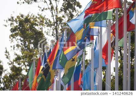 Flags of different countries waving in the wind against a clear sky in a public space during daytime Flags of different countries waving in the wind against a clear sky in a public space during daytime 141240626