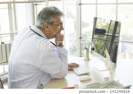 Orthopedic doctor working on his computer in his office. Orthopedic doctor with ankle bone structure model on table. Orthopedic doctor working on his computer in his office. Orthopedic doctor with ankle bone structure model on table. 141240826