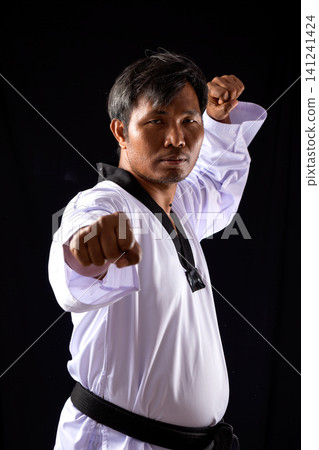 A taekwondo black belt demonstrates a powerful straight punch in a studio with a dark background, highlighting strength, precision, discipline, and self-defense skills 141241424