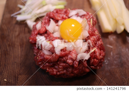 Raw Beef Patty with Egg Yolk and Onions on Cutting Board Raw Beef Patty with Egg Yolk and Onions on Cutting Board 141241796