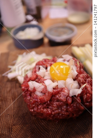 Raw Beef Patty with Egg Yolk and Onions on Cutting Board 141241797