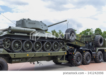 Side profile view of a vintage historic Soviet tank loaded onto a modern heavy-duty multi-axle tank transporter trailer. Side profile view of a vintage historic Soviet tank loaded onto a modern heavy-duty multi-axle tank transporter trailer. 141242098