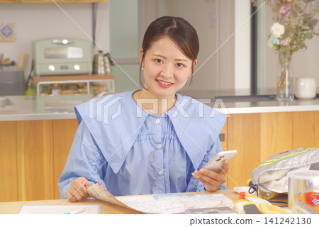 A woman checks her disaster preparedness supplies using her smartphone. 141242130