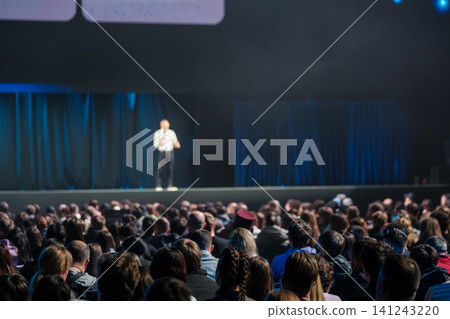 Speaker delivering keynote presentation to large audience at professional conference on stage Speaker delivering keynote presentation to large audience at professional conference on stage 141243220