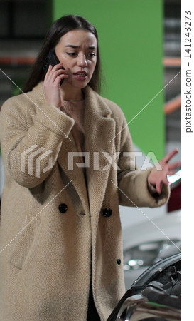 Vertical video Desperate woman stands by a broken car in the parking lot of shopping cent and calls the car service. Problems with the car. 141243273