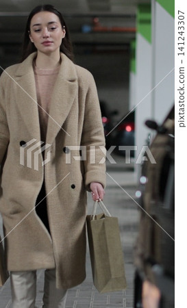 Vertical video Young woman walks through the parking lot of shopping center to car. Puts paper bags with purchases. Shopping, sale, discounts in stores. Vertical video Young woman walks through the parking lot of shopping center to car. Puts paper bags with purchases. Shopping, sale, discounts in stores. 141243307