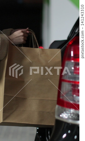 Vertical video Female opening rear door, putting purchases in paper bags into car. Shopping in city center. Shopping, sale, discounts in stores. Vertical video Female opening rear door, putting purchases in paper bags into car. Shopping in city center. Shopping, sale, discounts in stores. 141243310