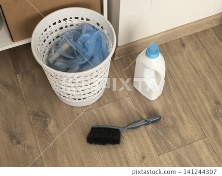 Plastic trash basket with bag detergent bottle and brush on wooden floor Plastic trash basket with bag detergent bottle and brush on wooden floor 141244307