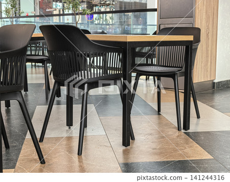 Modern black slatted armchairs and wooden table in food court interior Modern black slatted armchairs and wooden table in food court interior 141244316