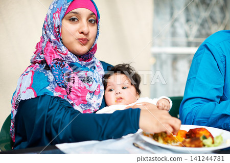 Mom, baby and muslim in table for dinner with food for eid, ramadan and religion to enjoy at home. Faith, Islam and happy with meal or supper from fasting on religious outfit with feast and family. Mom, baby and muslim in table for dinner with food for eid, ramadan and religion to enjoy at home. Faith, Islam and happy with meal or supper from fasting on religious outfit with feast and family. 141244781