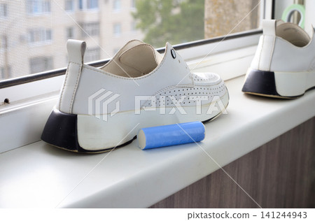 Blue cleaning stick for white shoes on windowsill, stain remover bar near leather sneakers by window in home interior 141244943