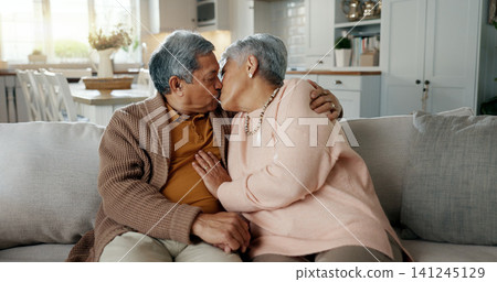 Happy, senior couple and a kiss on the sofa for love, relax and a hug in a house. Together, smile and an elderly man and woman with care, comfort and romance in a marriage on the living room couch 141245129