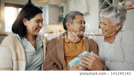 Birthday, gift and senior parents on sofa for celebration, festive event and bonding together at home. Happy family, party and elderly mother and father with daughter for present, surprise and love 141245143