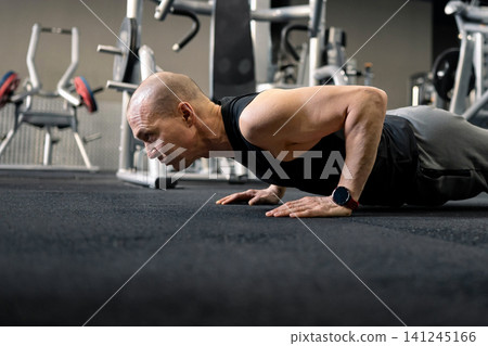 Athletic man performing push up exercise on gym floor 141245166