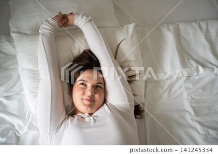 Young woman relaxing while stretching in bed as part of her morning routine. Sleep wellness and a healthy lifestyle focused on positive awakening and comfort Young woman relaxing while stretching in bed as part of her morning routine. Sleep wellness and a healthy lifestyle focused on positive awakening and comfort 141245334