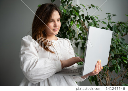 Focused woman using a laptop in a cozy home office environment. Remote work digital productivity and flexible workspace Focused woman using a laptop in a cozy home office environment. Remote work digital productivity and flexible workspace 141245346