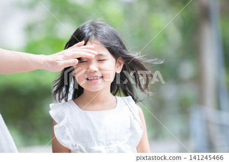 小女孩微笑著,媽媽的手放在她的額頭上。 小女孩微笑著,媽媽的手放在她的額頭上。 141245466