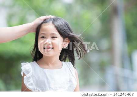 A little girl smiles with her mother's hand on her forehead. A little girl smiles with her mother's hand on her forehead. 141245467
