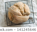 Freshly baked artisan sourdough knot bread loaf cooling down on a black metal wire rack. Top down overhead view on a rustic wooden table background. Perfect for baking process and bakery concept 141245646