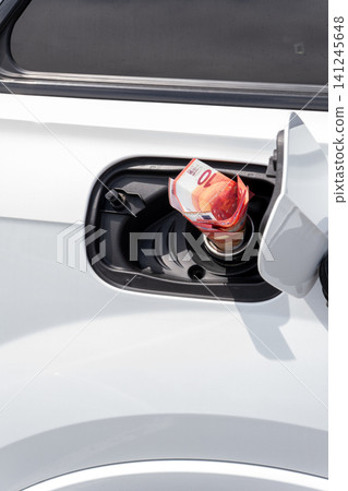 Rolled fifty Euro cash note inside vehicle fuel filler neck. Close-up view of white auto gas tank compartment with money symbolizing high petrol prices, inflation, and expensive transportation. Rolled fifty Euro cash note inside vehicle fuel filler neck. Close-up view of white auto gas tank compartment with money symbolizing high petrol prices, inflation, and expensive transportation. 141245648