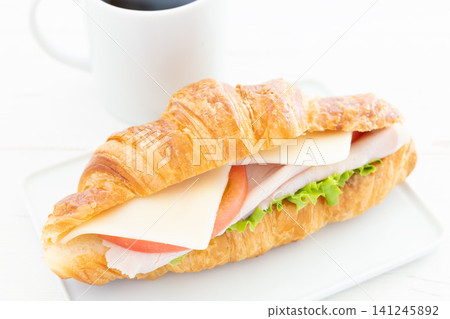 A delicious croissant sandwich with roast ham, fresh vegetables, and mozzarella, served with coffee for breakfast. A delicious croissant sandwich with roast ham, fresh vegetables, and mozzarella, served with coffee for breakfast. 141245892