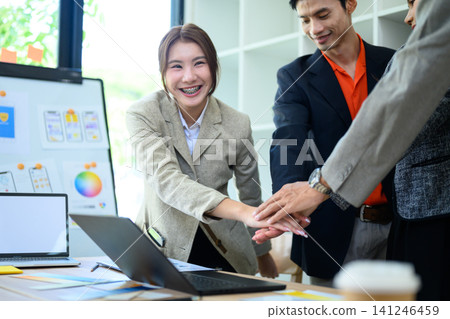 Asian Business Team Stacking Hands Together in Office Meeting Room Showing Unity and Teamwork 141246459