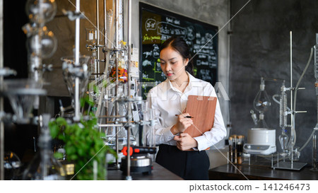 Young Asian Female Scientist Taking Notes on Clipboard in Modern Laboratory with Glass Distillation Equipment Young Asian Female Scientist Taking Notes on Clipboard in Modern Laboratory with Glass Distillation Equipment 141246473